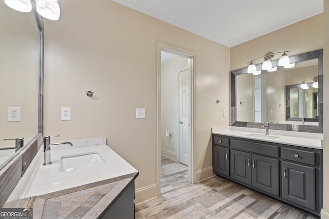 bathroom with wood finished floors, two vanities, a sink, and baseboards