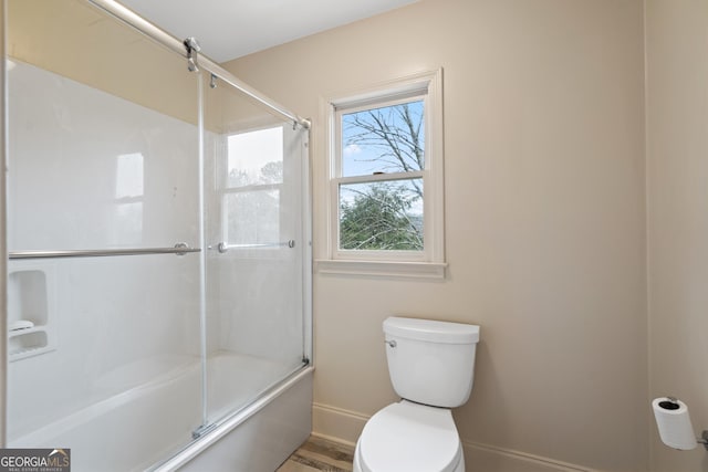 bathroom with baseboards, shower / bath combination with glass door, and toilet