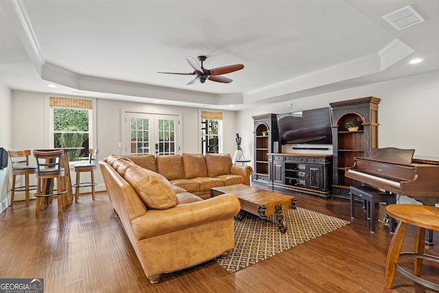 living area with a tray ceiling, wood finished floors, and visible vents