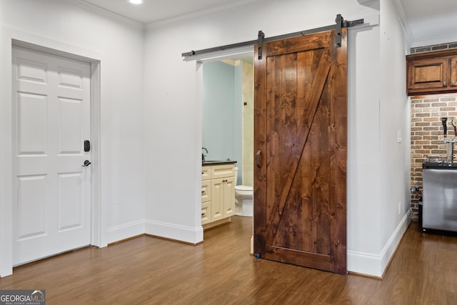 interior space with a barn door, ornamental molding, and wood finished floors