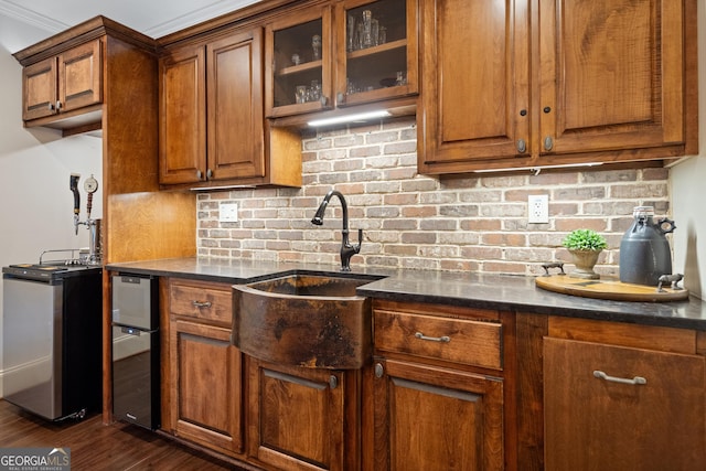 kitchen with a sink, tasteful backsplash, brown cabinetry, dark wood finished floors, and glass insert cabinets