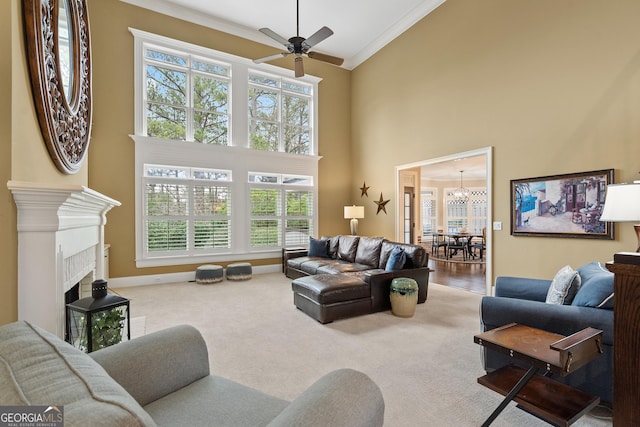 living room with a tiled fireplace, a high ceiling, carpet flooring, baseboards, and ceiling fan with notable chandelier