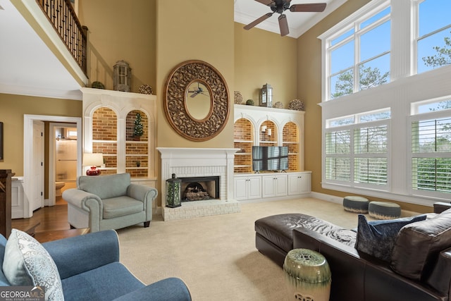 living room with ornamental molding, a brick fireplace, a towering ceiling, and a healthy amount of sunlight