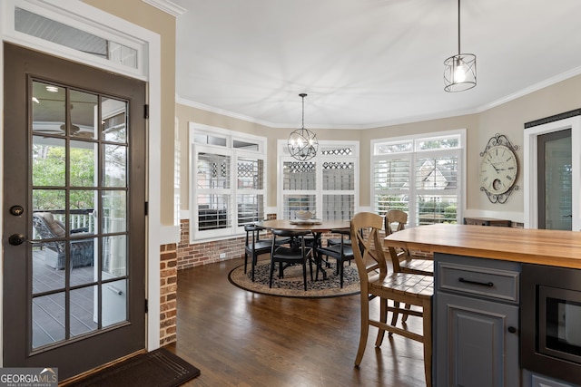 dining space featuring dark wood-style floors, brick wall, crown molding, and an inviting chandelier