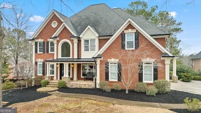 view of front facade featuring covered porch, brick siding, and roof with shingles