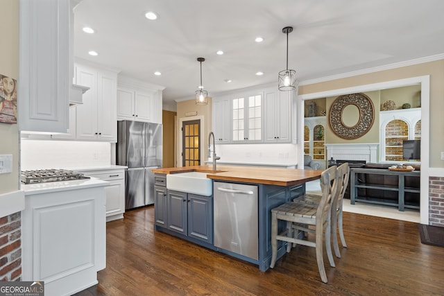 kitchen with butcher block countertops, a sink, white cabinetry, appliances with stainless steel finishes, and a center island with sink