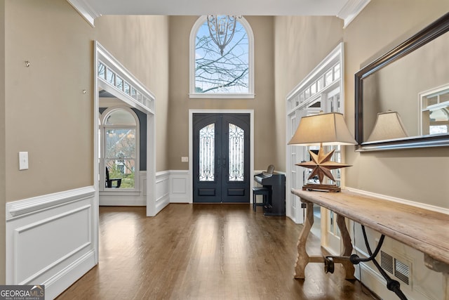 foyer with french doors, visible vents, a decorative wall, wainscoting, and wood finished floors