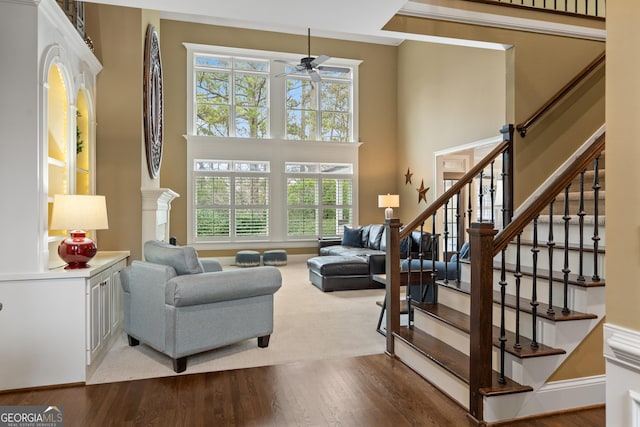 living area featuring a ceiling fan, stairs, a high ceiling, and wood finished floors