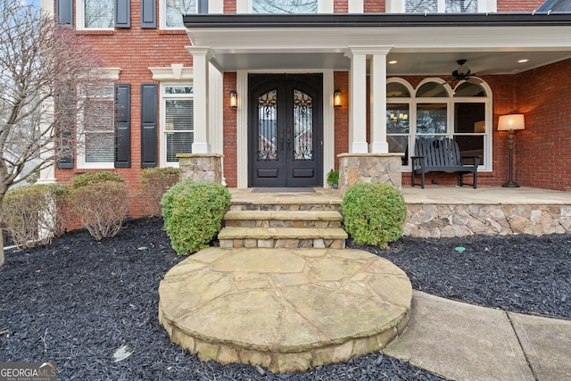 property entrance featuring covered porch, ceiling fan, brick siding, and french doors