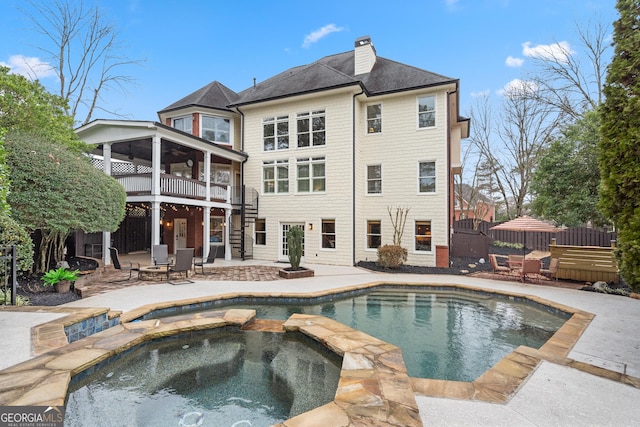 rear view of house featuring a chimney, stairway, fence, a patio area, and a pool with connected hot tub