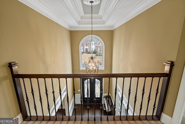 staircase featuring baseboards, wood finished floors, a tray ceiling, crown molding, and a notable chandelier