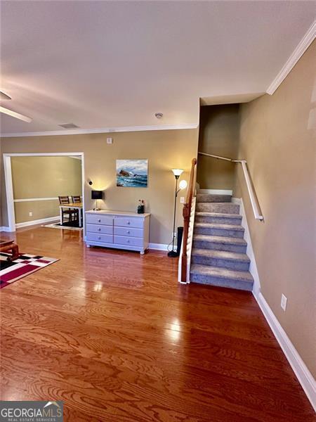 unfurnished living room featuring ornamental molding, stairway, baseboards, and wood finished floors