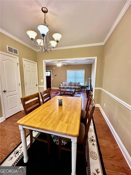 dining room with dark wood finished floors, visible vents, crown molding, and baseboards