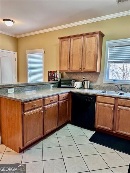 kitchen with brown cabinetry, black dishwasher, a sink, and a peninsula