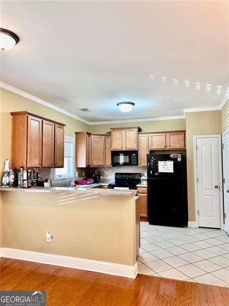 kitchen with black appliances, light wood finished floors, a peninsula, and light countertops