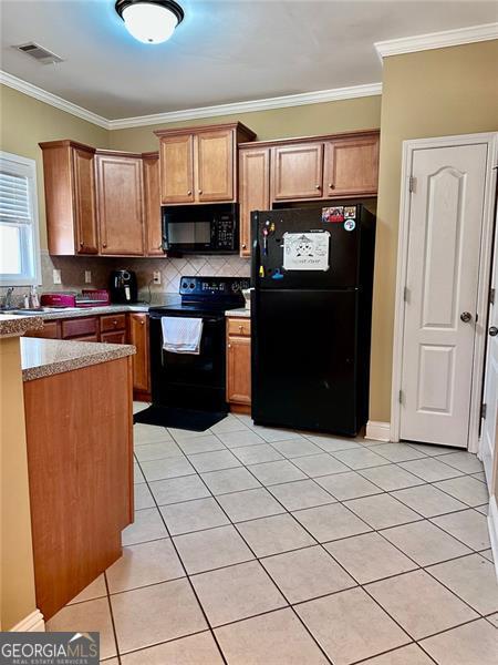 kitchen featuring black appliances, brown cabinetry, light tile patterned flooring, and crown molding