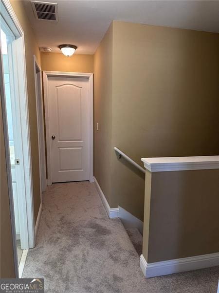 corridor featuring baseboards, an upstairs landing, visible vents, and light colored carpet