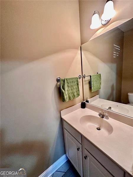 half bathroom with tile patterned floors, vanity, toilet, and baseboards