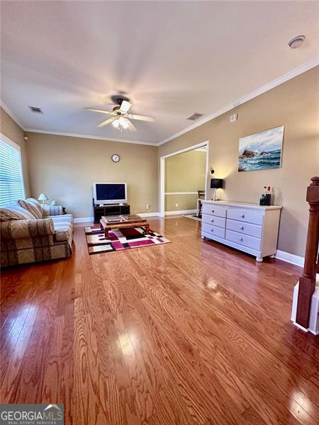 living room with baseboards, visible vents, ornamental molding, and wood finished floors