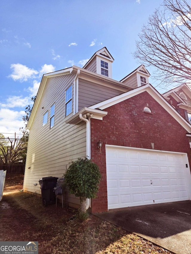 view of side of property featuring driveway, an attached garage, fence, and brick siding