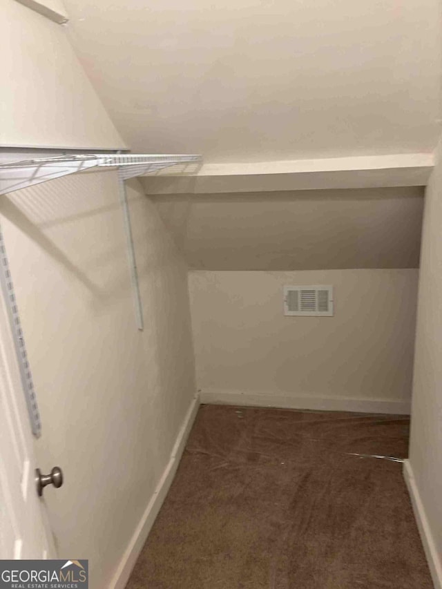 spacious closet featuring vaulted ceiling, visible vents, and dark carpet