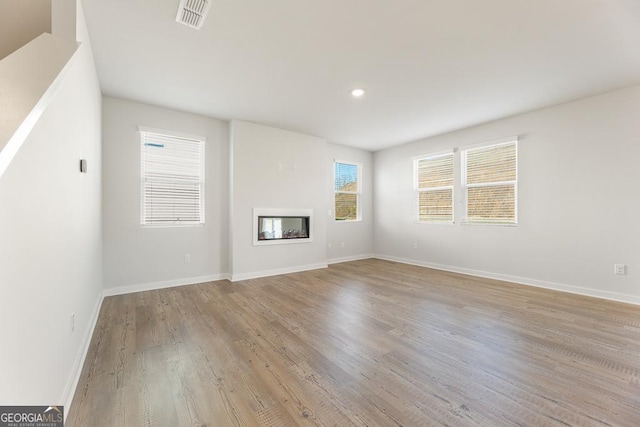 unfurnished living room with light wood-style flooring, recessed lighting, visible vents, baseboards, and a glass covered fireplace