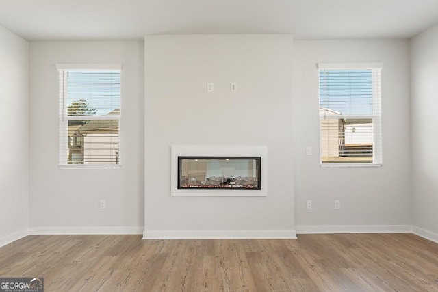 unfurnished living room with a glass covered fireplace, baseboards, plenty of natural light, and light wood finished floors