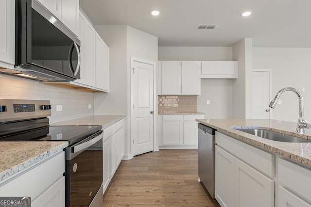 kitchen featuring a sink, visible vents, white cabinetry, appliances with stainless steel finishes, and light stone countertops