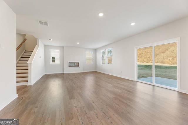 unfurnished living room featuring light wood-style floors, baseboards, stairway, and visible vents