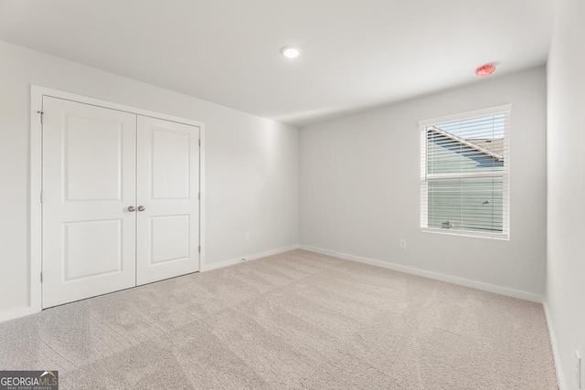 unfurnished bedroom with a closet, light colored carpet, and baseboards