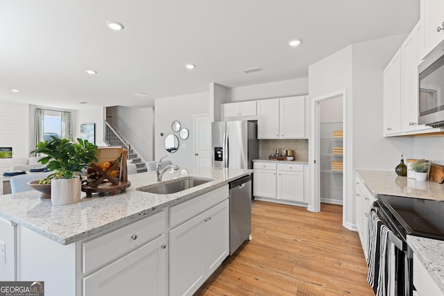 kitchen with stainless steel appliances, white cabinets, a sink, and a center island with sink