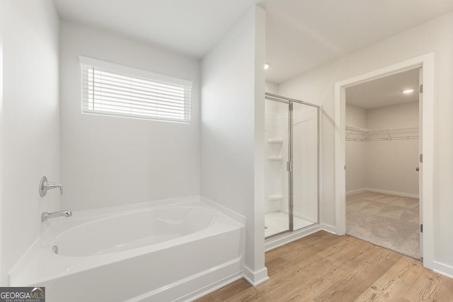 full bathroom with a walk in closet, a garden tub, a shower stall, wood finished floors, and baseboards