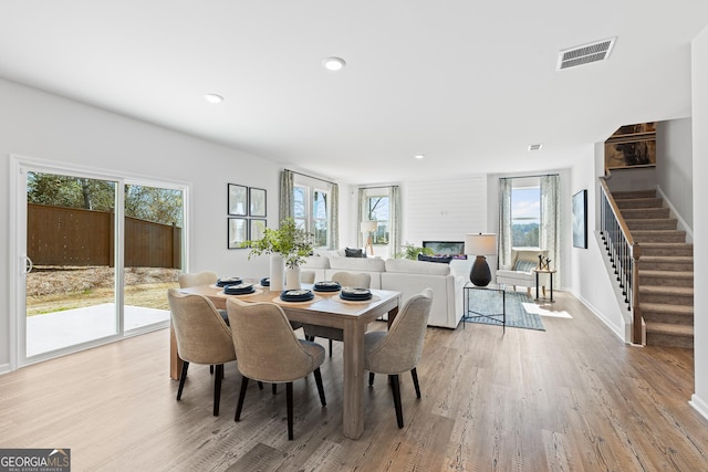 dining room with light wood finished floors, visible vents, a glass covered fireplace, stairway, and recessed lighting