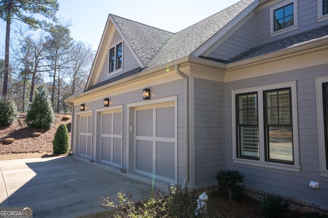 view of side of home featuring a garage, concrete driveway, and roof with shingles