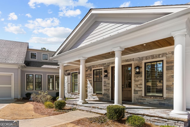 doorway to property featuring an attached garage, stone siding, and a porch