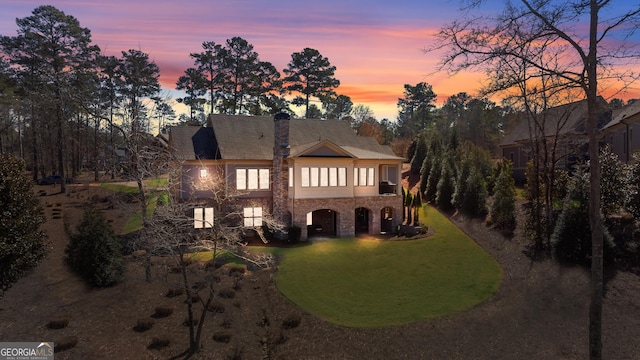 view of front of house with stone siding, a lawn, and a chimney