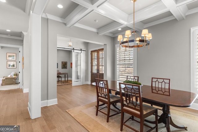 dining space featuring a barn door, baseboards, coffered ceiling, light wood-style flooring, and beam ceiling