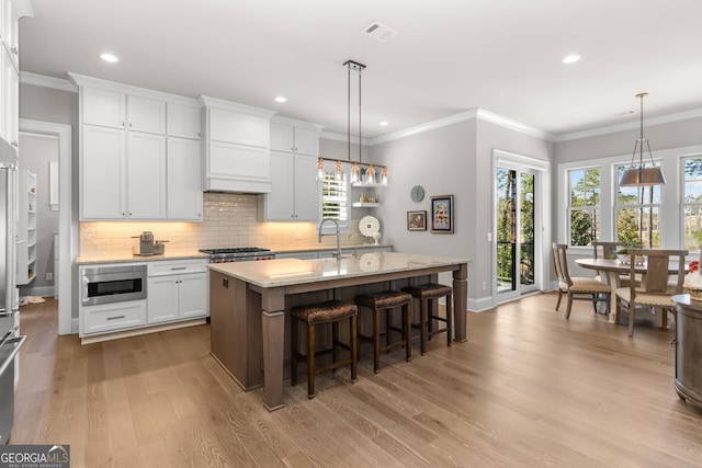 kitchen with a center island with sink, visible vents, appliances with stainless steel finishes, white cabinetry, and pendant lighting