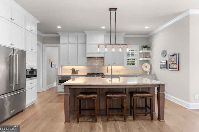 kitchen with high end fridge, white cabinetry, a center island with sink, and open shelves