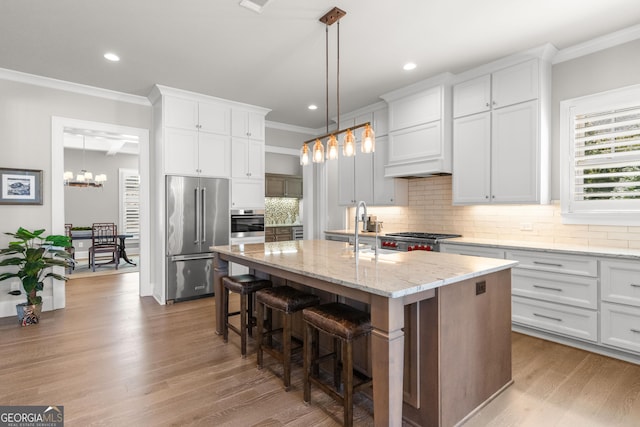 kitchen with stainless steel appliances, white cabinetry, a center island with sink, and light stone counters