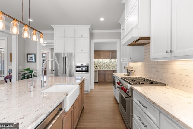 kitchen featuring premium appliances, hanging light fixtures, light stone countertops, white cabinetry, and a sink