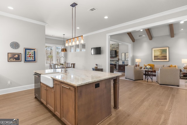 kitchen with a center island with sink, hanging light fixtures, light wood-style flooring, open floor plan, and a sink