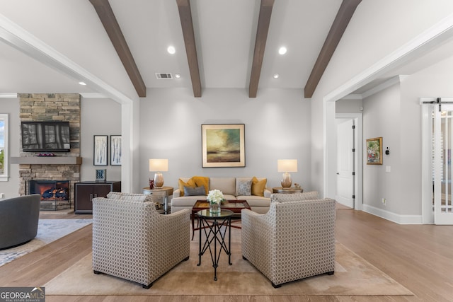 living room with a stone fireplace, visible vents, baseboards, light wood finished floors, and beamed ceiling