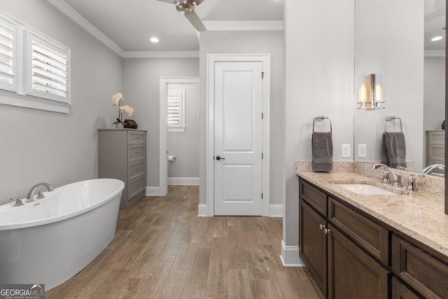 bathroom featuring crown molding, vanity, wood finished floors, a freestanding tub, and baseboards