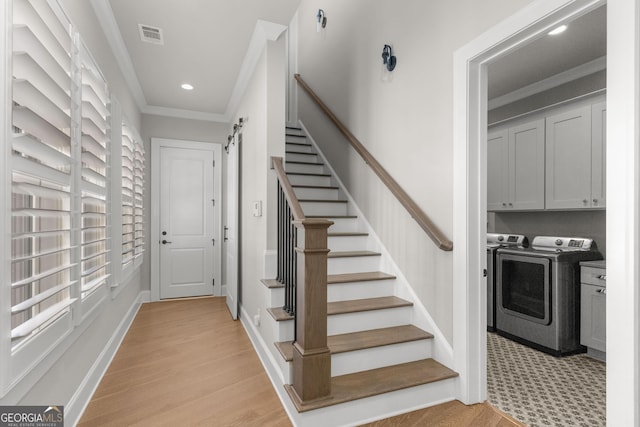 staircase with a barn door, wood finished floors, washing machine and clothes dryer, crown molding, and recessed lighting