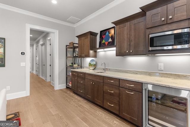 kitchen with dark brown cabinetry, wine cooler, stainless steel microwave, crown molding, and a sink