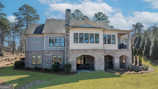 rear view of property featuring a balcony, a chimney, a lawn, and brick siding