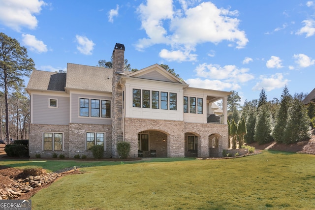 back of property with a shingled roof, a chimney, a lawn, and brick siding