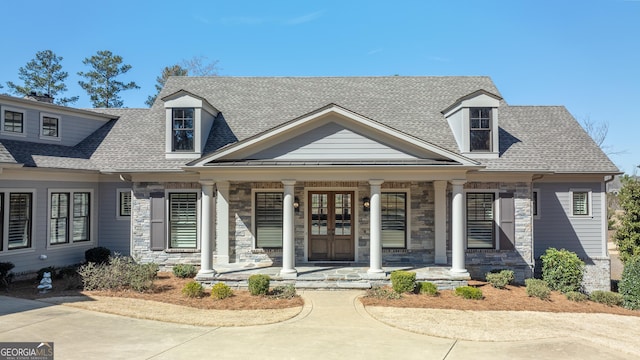 cape cod home featuring a shingled roof, covered porch, french doors, and stone siding