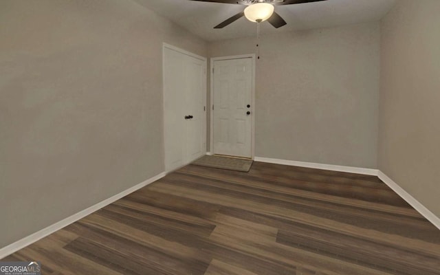 spare room featuring dark wood-type flooring, a ceiling fan, and baseboards